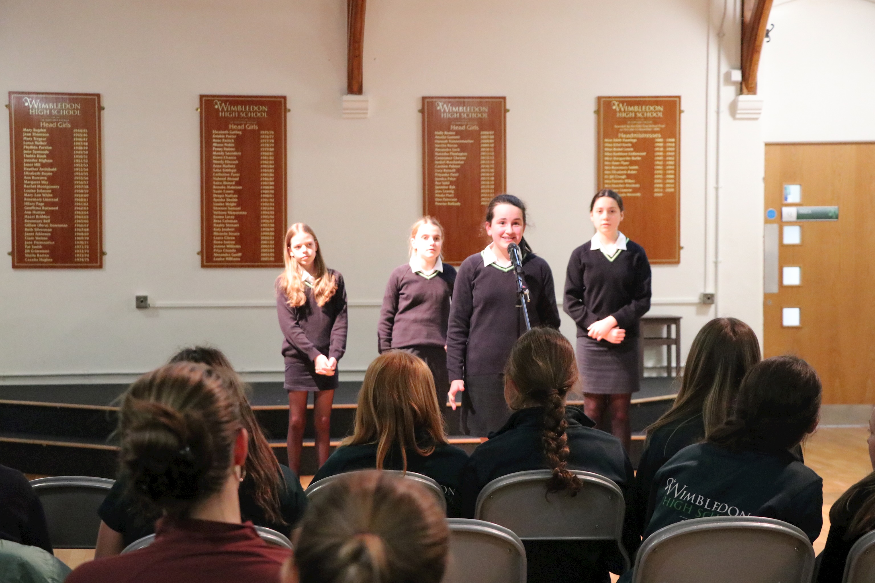 Students in the senior school taking part in Poetry by Heart. They are standing in Senior Hall reciting a poem to a room of students and teachers