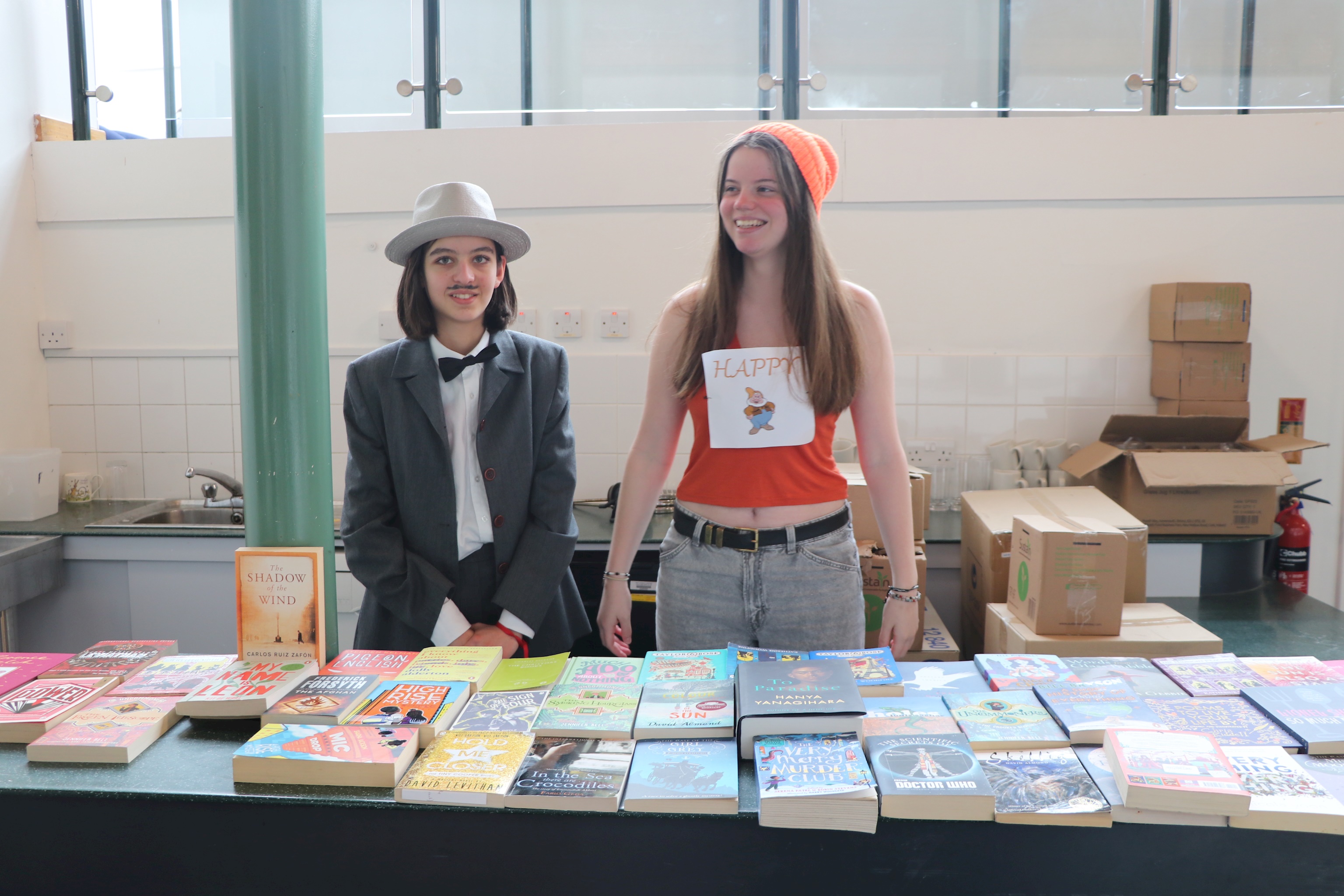 Two sixth form students standing behind a book stall, running the World Book Day book swap