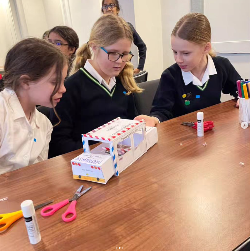 Junior school pupils sitting at a table and making a car out of paper